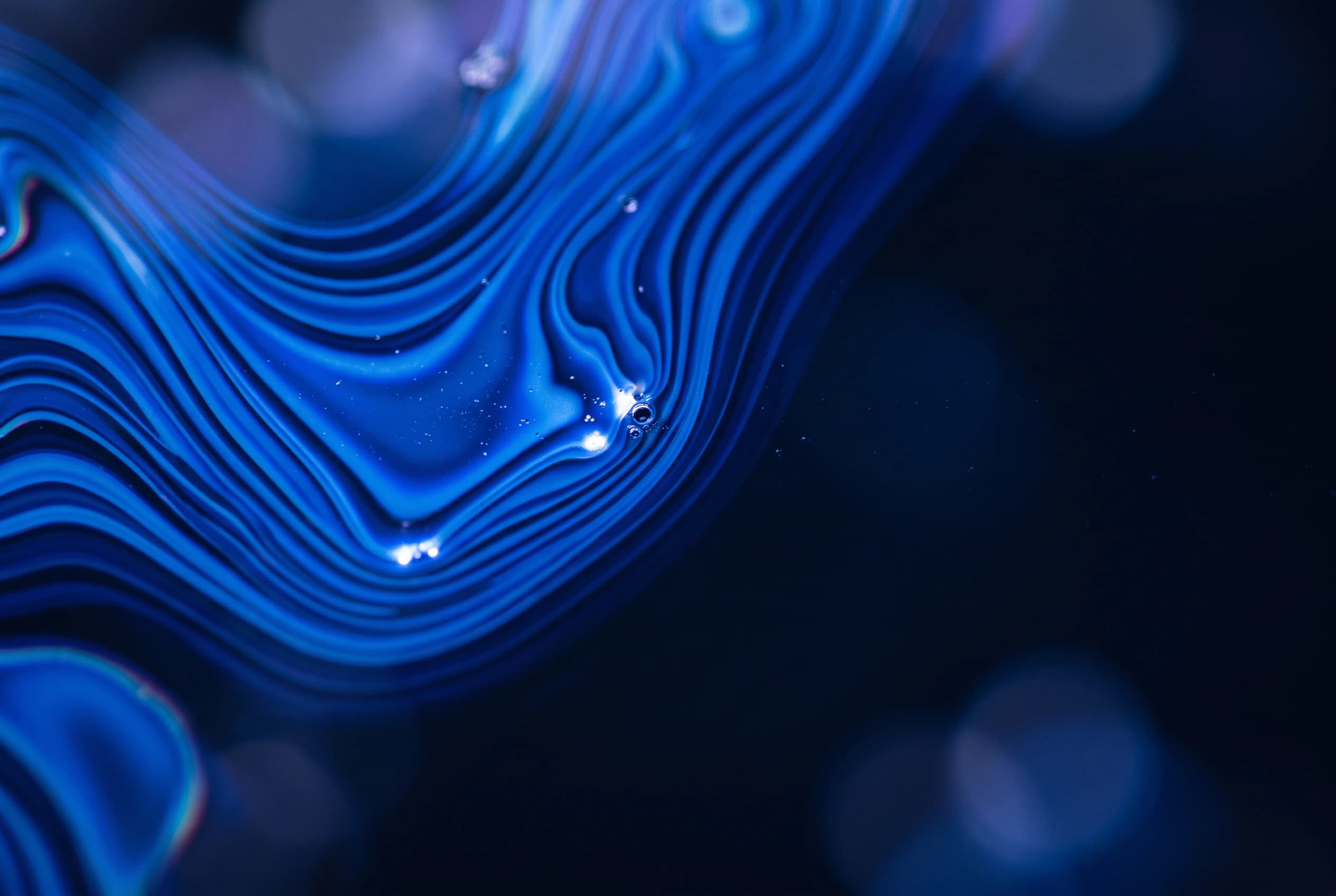 Rippling blue contours like liquid, with small bright droplets, on a dark background