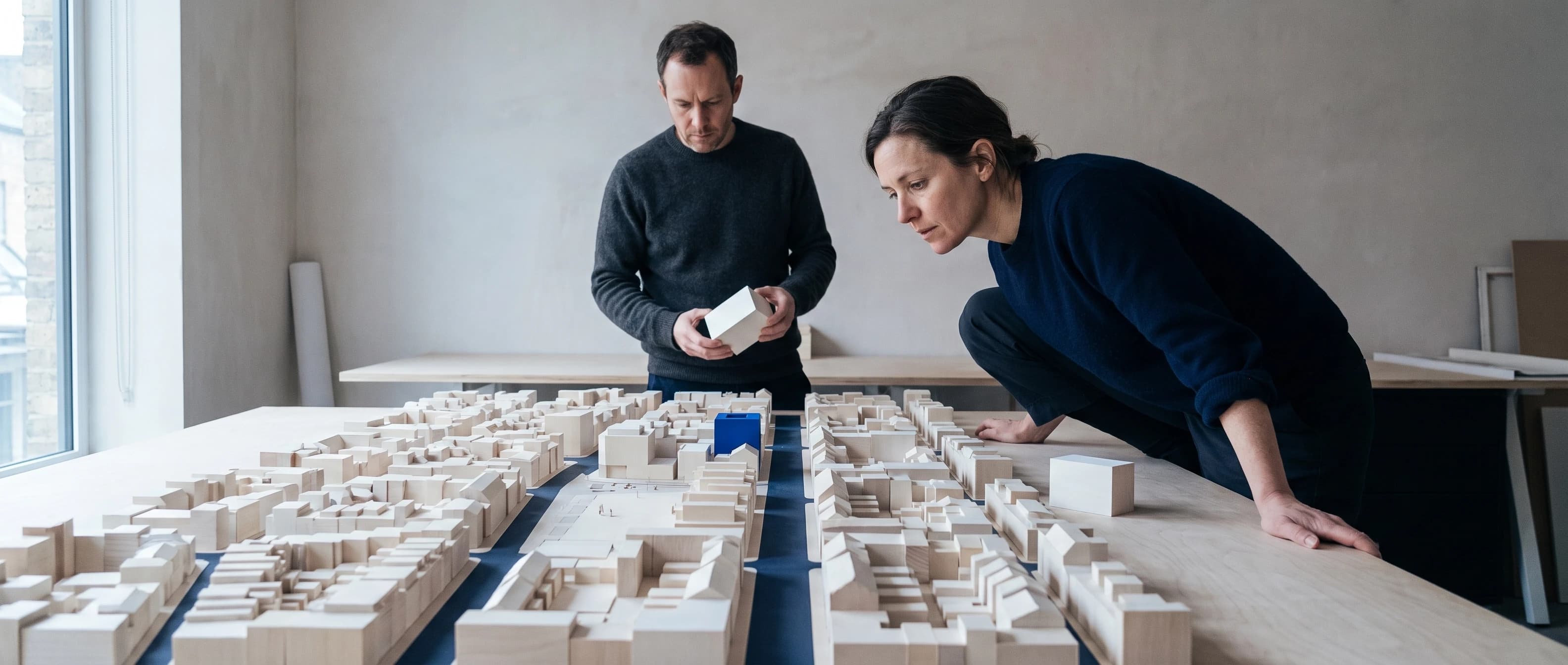 Two architects leaning over a white massing model of a city block