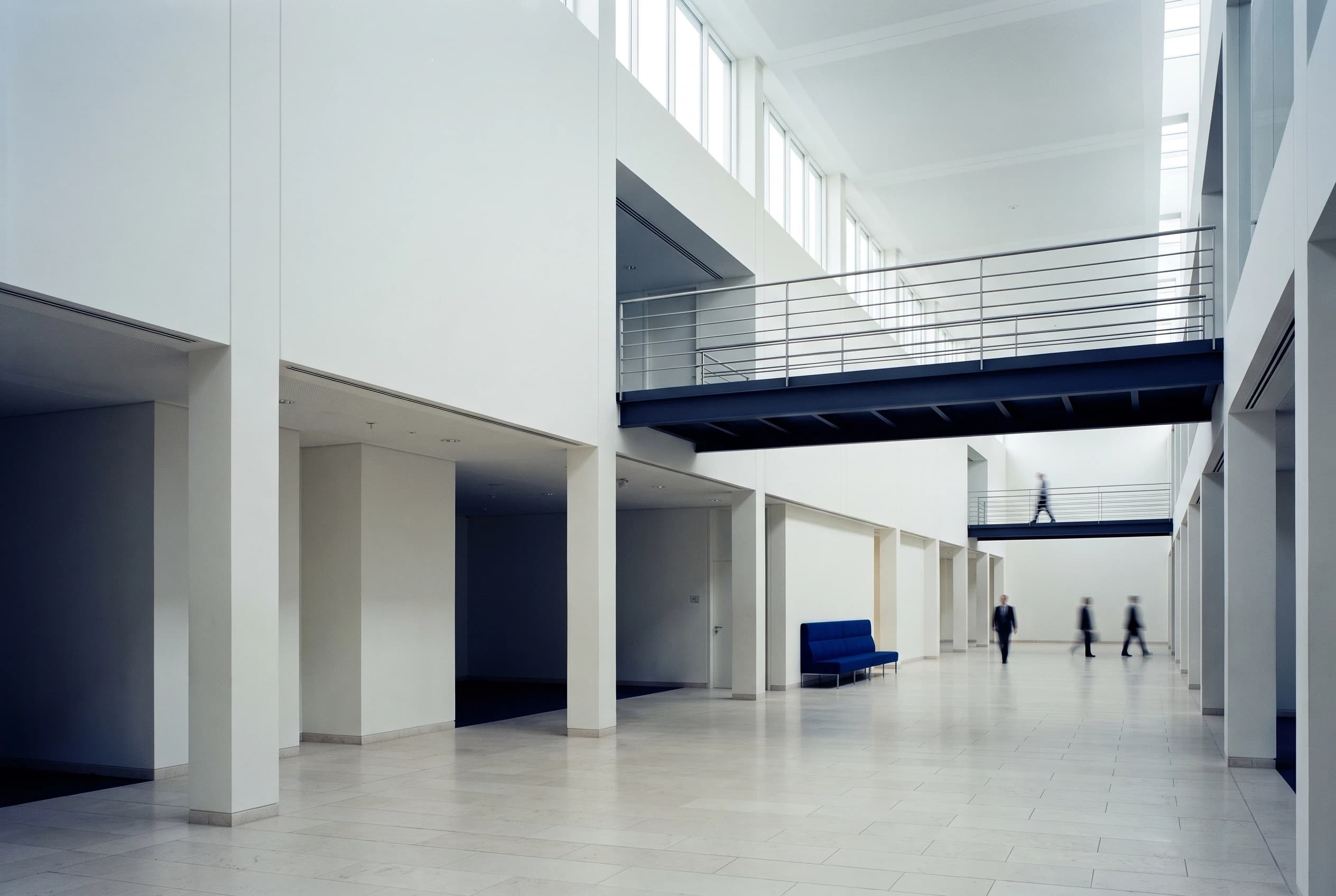 A bright double-height atrium with a steel bridge and people walking below