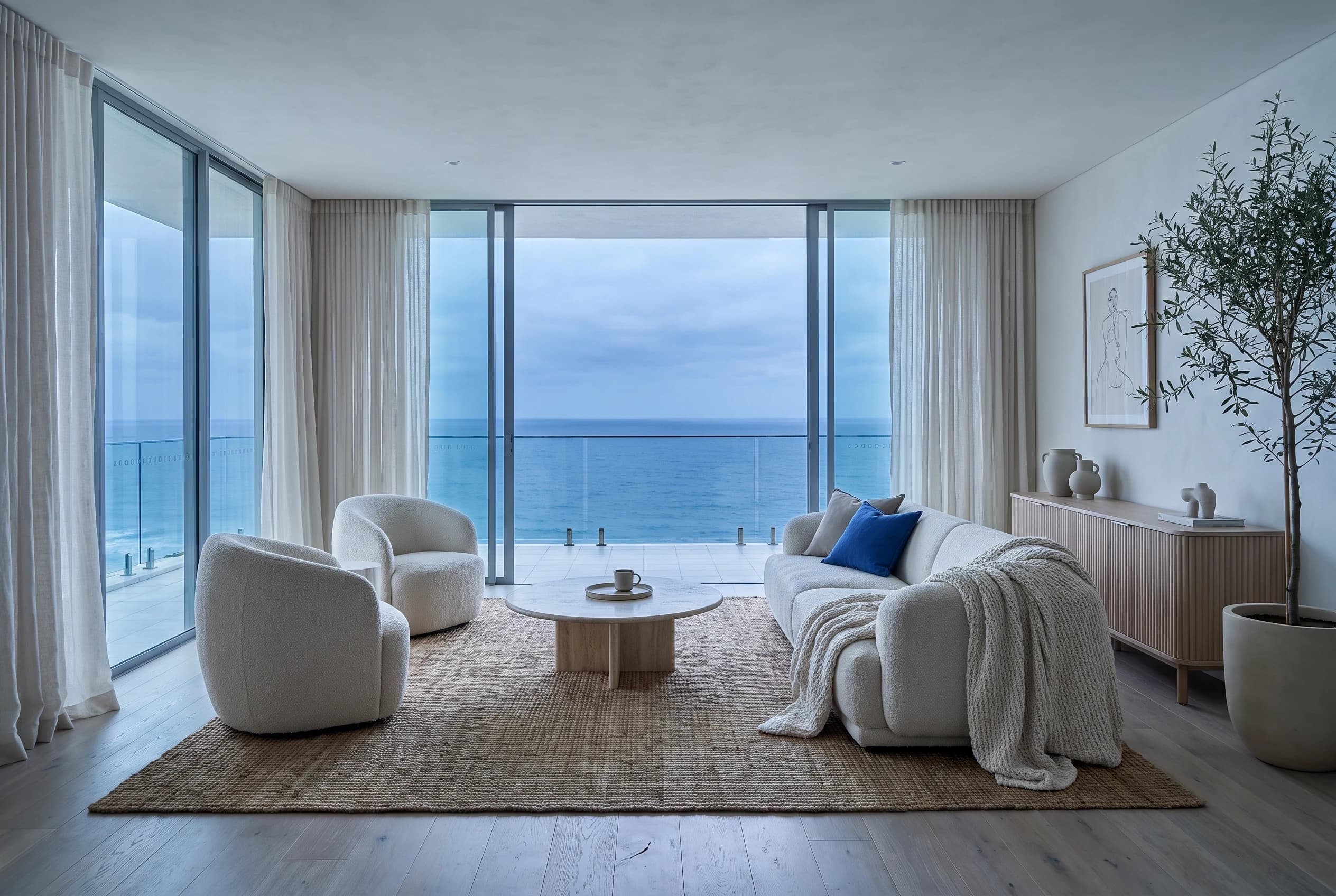 A calm living room with white furniture and floor-to-ceiling views of the sea