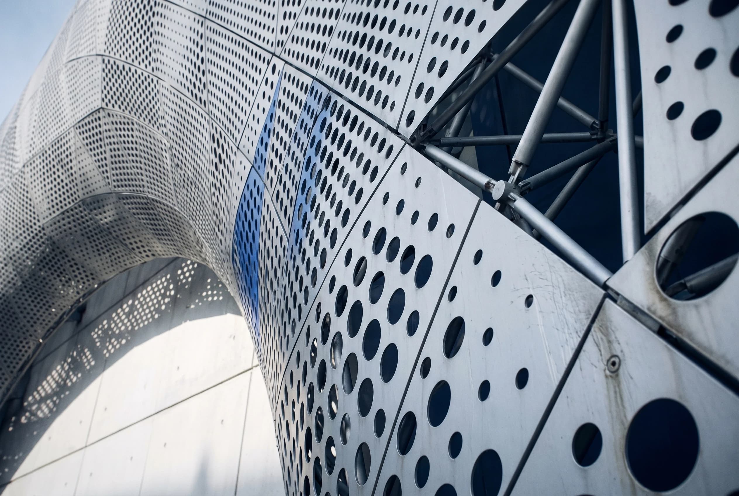 Looking up at a curved perforated metal facade on a steel frame