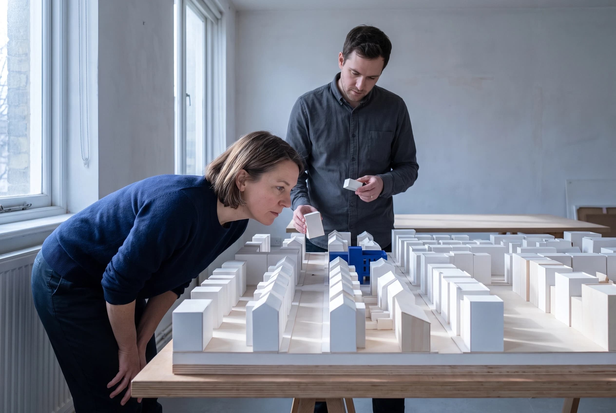Two people placing blocks on a white masterplan model, one in blue