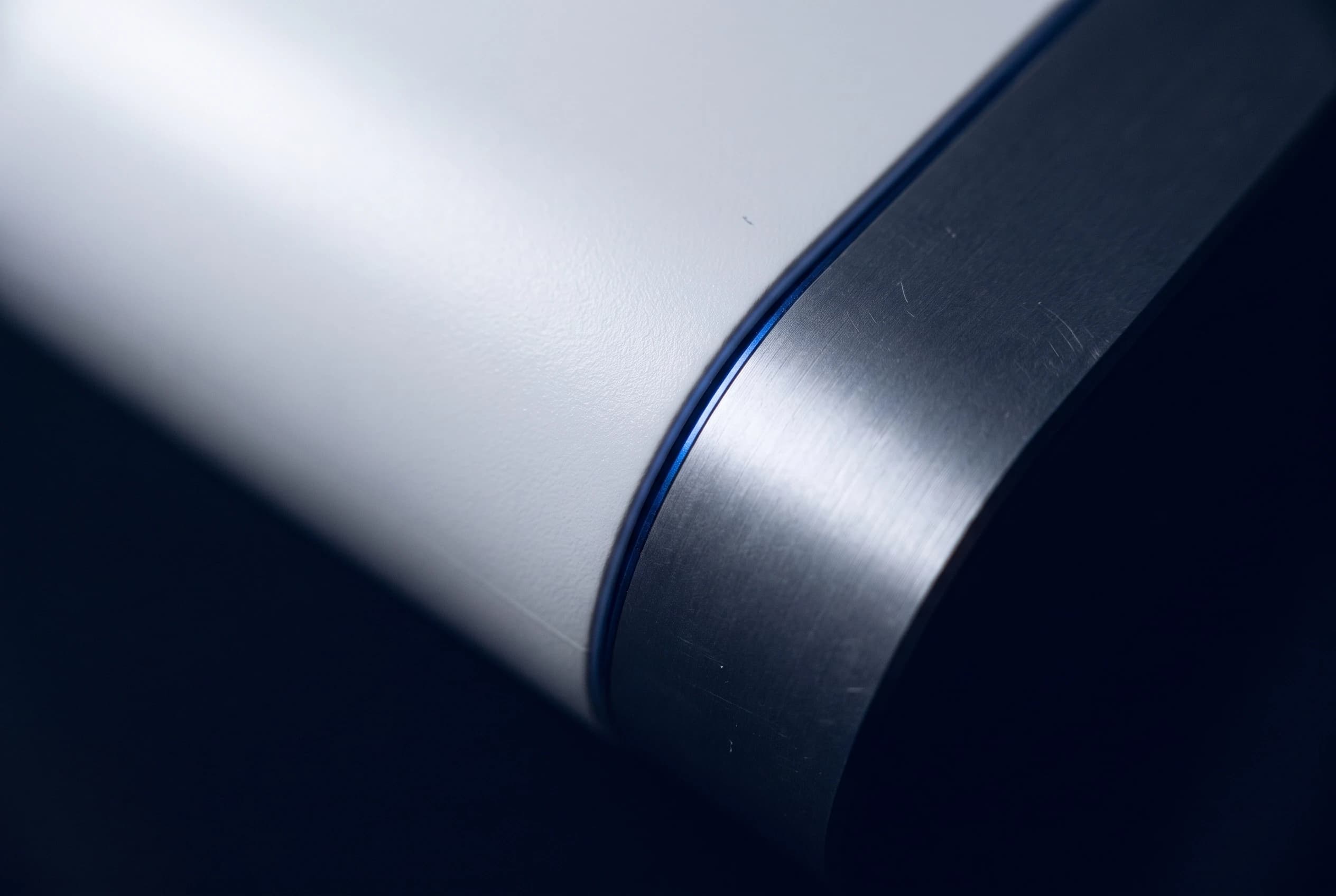 Close-up of a white product edge meeting brushed metal along a blue seam