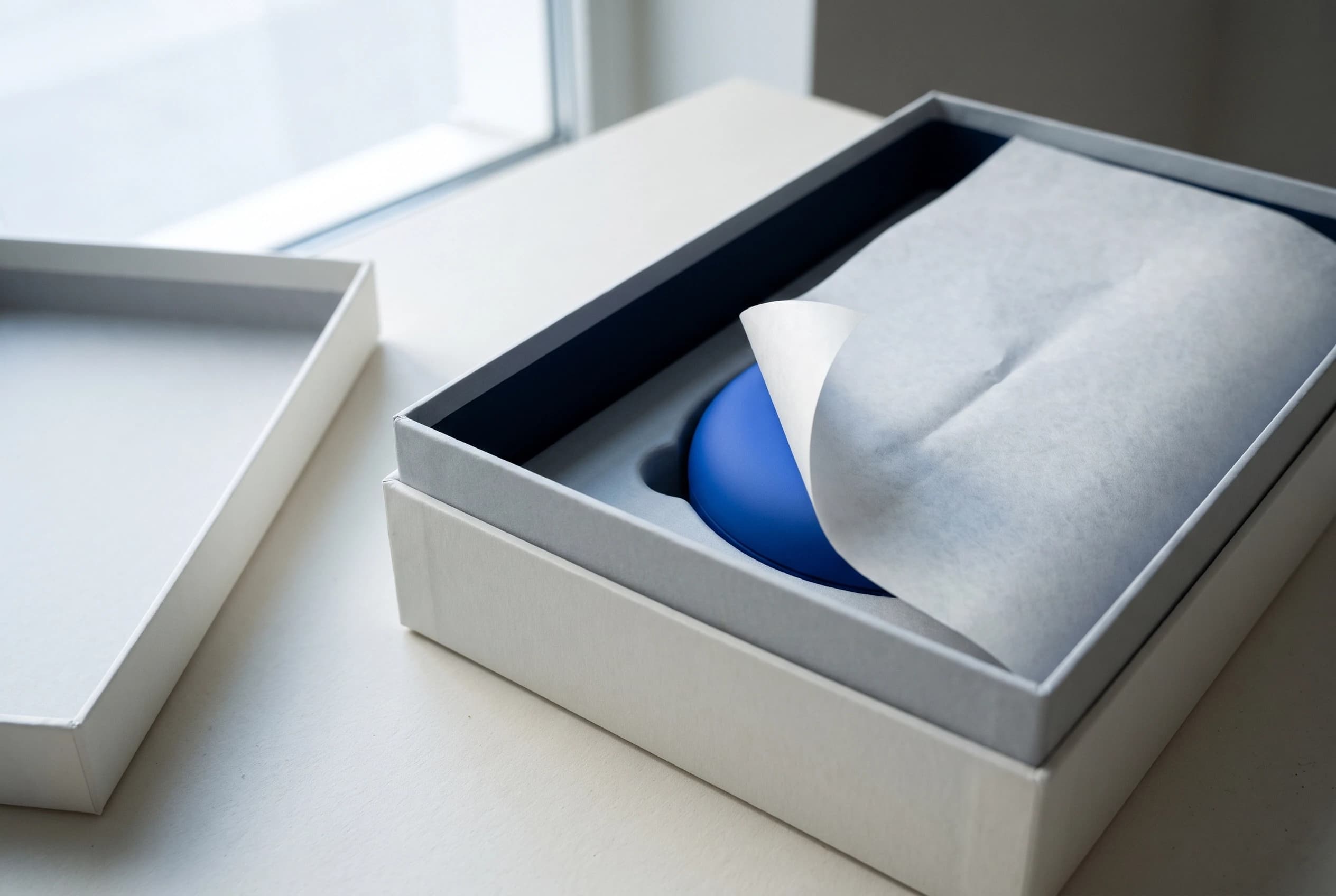A rigid box opened to show a blue product under tissue paper