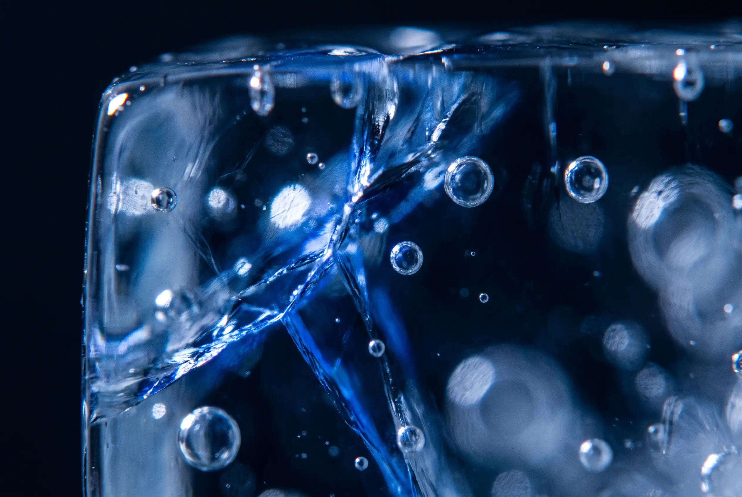 Close-up of a cracked, clear block with trapped bubbles, lit deep blue