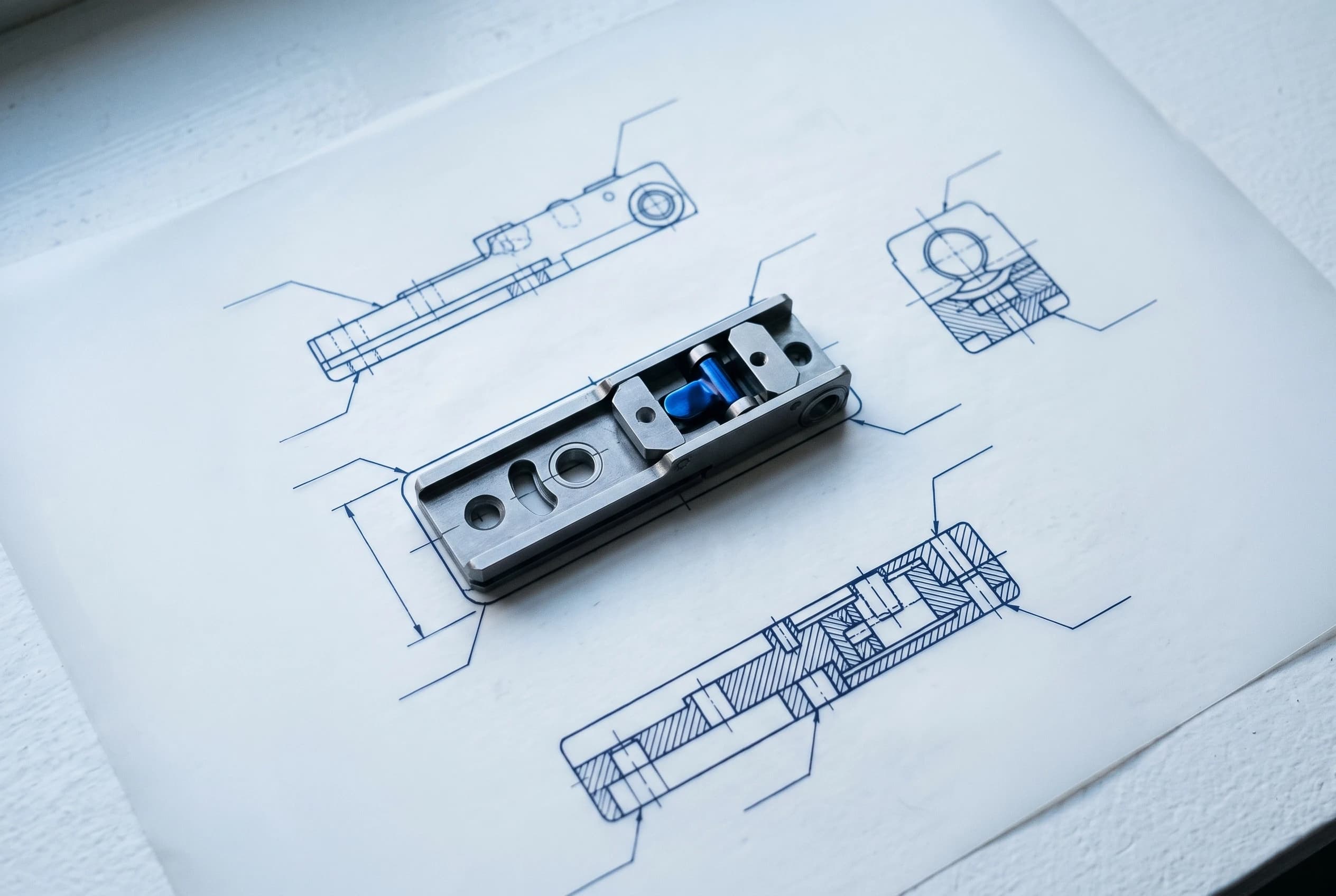 A machined part resting on blue-line patent drawings of itself