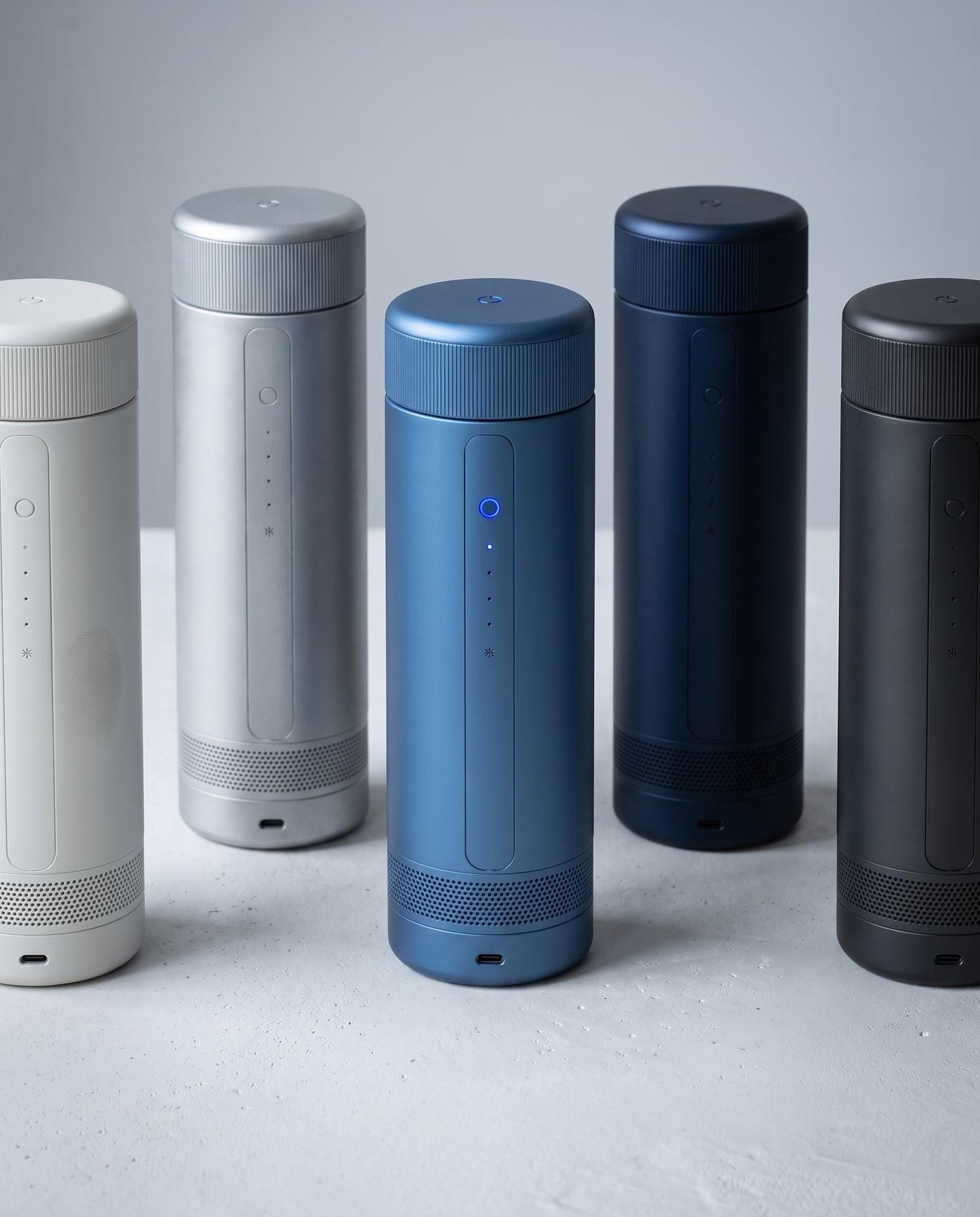 Five CELSIUS ONE units staggered on a white surface in white, silver, blue, navy and charcoal, each cap matching its body, the blue unit lit