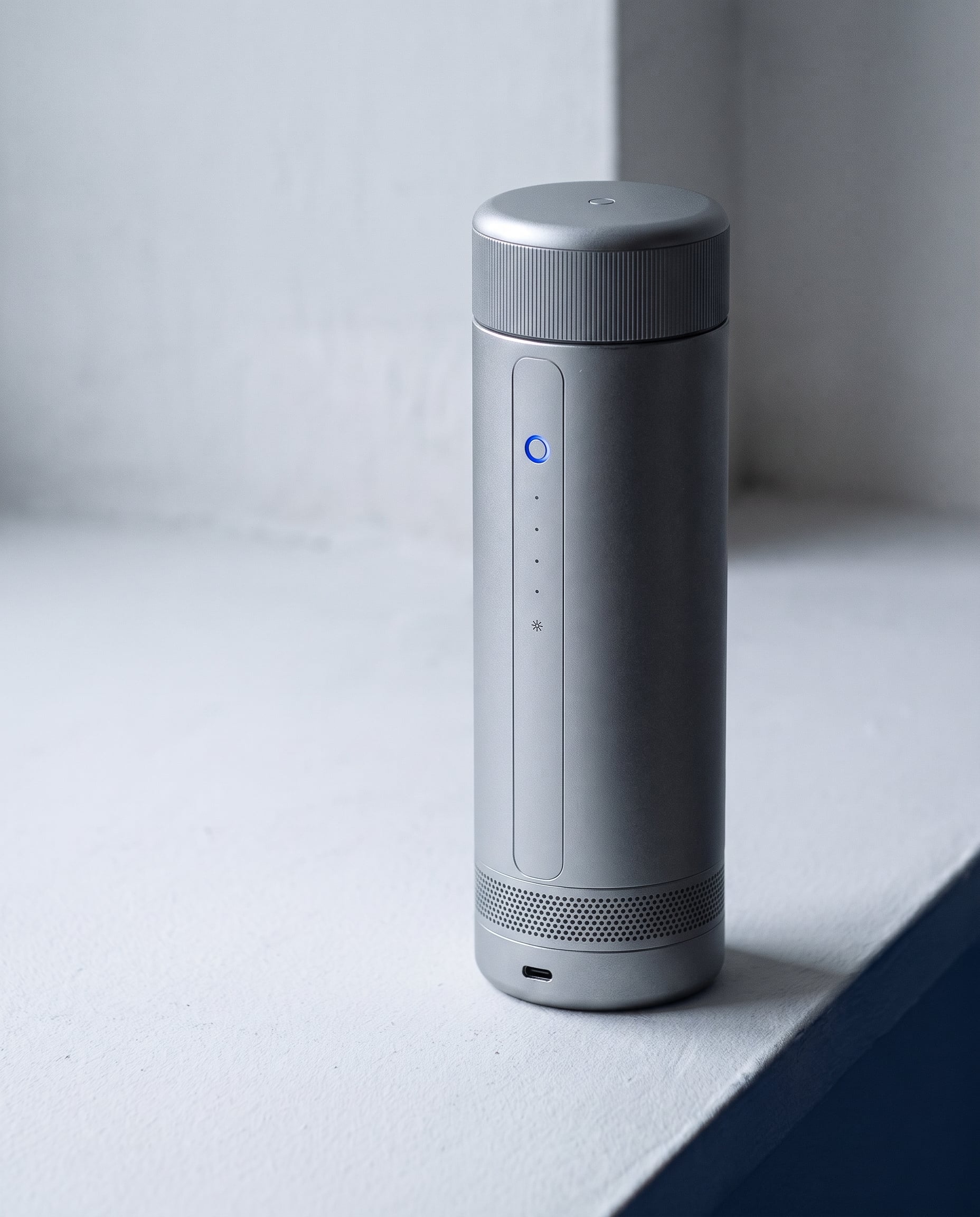 A silver CELSIUS ONE on a white ledge: the flush control spine with a lit blue ring, four gauge dots and a snowflake mode icon, above a perforated base band and a USB-C port