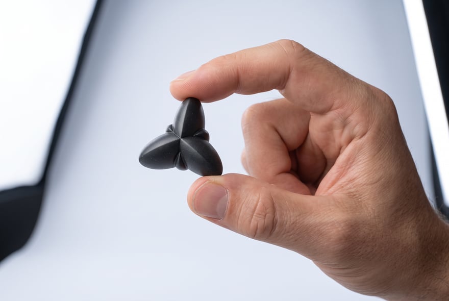 Render of a thumb and forefinger pinching a single Oberon module, its three lobes and blade-fins facing the camera