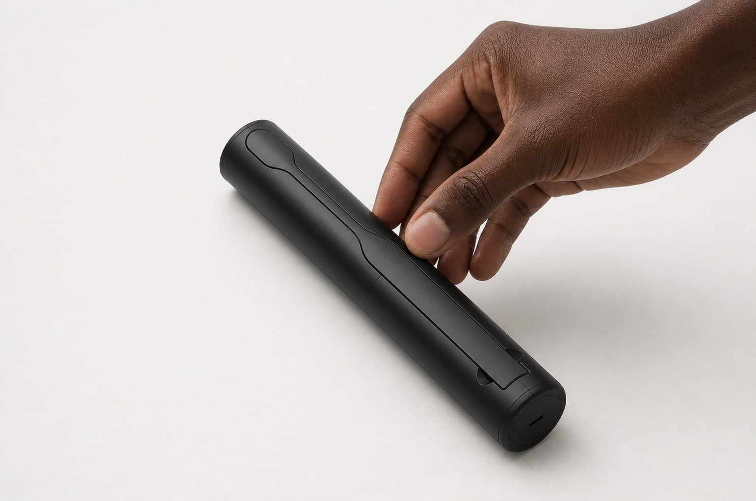 Render of the closed case lying on a pale surface as a hand reaches down to lift it, showing its size against the fingers